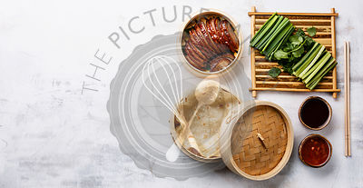 Sliced Peking Duck in bamboo steamer served with fresh cucumber, green onions, cilantro and roasted wheaten chinese pancakes with sauce Hoysin on white background copy space