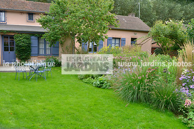 Jardin en automne : pelouse et massif fleuri : Pennisetum spp. (Herbe aux écouvillons), maison. Jardin du peintre André Van Beek, Saint-Paul (60), France