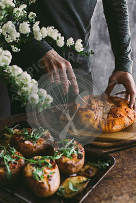 Man's hand cutting bread on wooden board. Preparation for lunch. Rustic backgraund