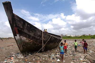 Plastic garbage lines the beach near an abandoned wooden boat, Juhu Beach, Mumbai, India.