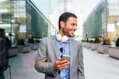 Smiling businessman with headphones and cell phone in the city