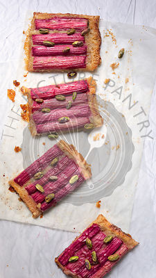 A rectangular rhubarb tart sprinkled with pistachio nuts and cut into pieces.
