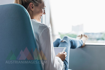Smiling woman sitting by the window with feet up using tablet