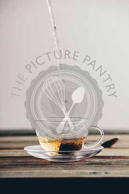 Pouring hot water into glass cup with tea bag on wooden table background