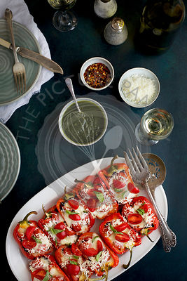 Black Rice Caprese Stuffed Roasted Red Peppers served with a fresh Basil Oil and white wine. Photographed from top view on a dark blue background.