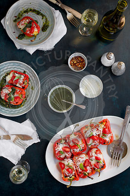 Black Rice Caprese Stuffed Roasted Red Peppers served with a fresh Basil Oil and white wine. Photographed from top view on a dark blue background.