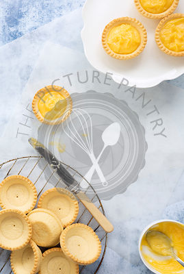 Unfilled pastry cases on a wire rack and lemon tartlets on a plate.
