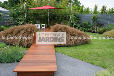 Jardin contemporain. Dallage bois. Passage surélevé. Carex comans 'Milk Chocolate'. Coin repos. Voile d'ombrage. Parasol. Irlande. Paysagistes : Com Doyle et Dean Lacey
