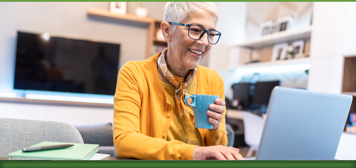Woman wearing yellow shirt and glasses drinking coffee while on laptop