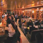 A bunch of people gather at the bar and in booths of the Brandy Library.