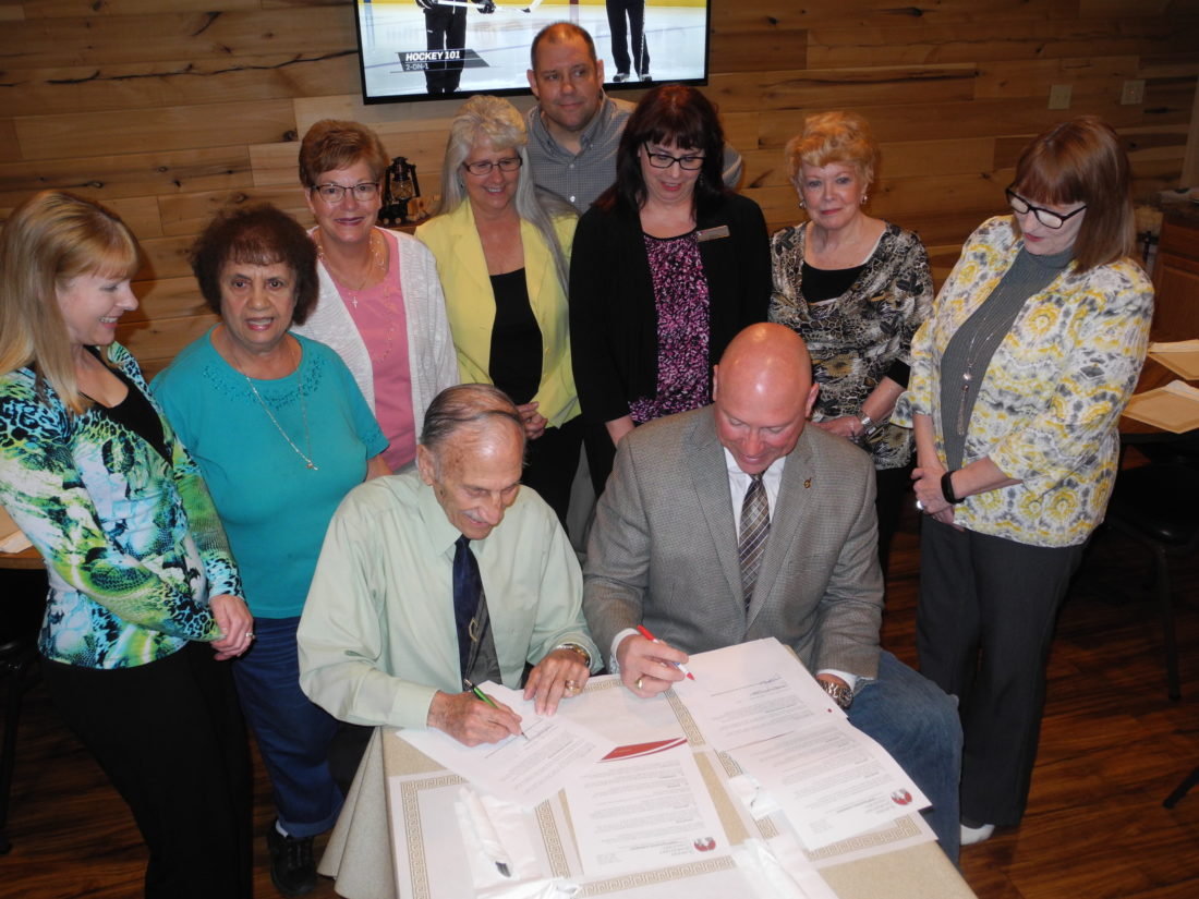 PARTNERSHIP FORMED — Members of the Follansbee Chamber of Commerce watch as Chamber President Tony Paesano, seated left, signs agreements with Pat Ford, executive director of the Business Development of the Northern Panhandle; calling for the chamber to serve as its task force for economic development in the city and a Good Neighbor Agreement involving the former Follansbee Steel property owned by the economic development group. Behind Paesano and Ford are, from left, Brandy Puskarich, Carmel Esposito, Charlotte Kolenc, Olive McGee, Vito “Skip” Cutrone, Alexis Pace, Pat Accettolo and Debbie Puskarich. -- Warren Scott