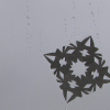 Square icon with dark grey, clouding sky in the background and a paper snowflake and raindrops on a glass pane in the foreground.