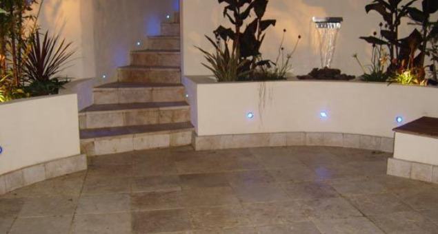 We created a large circular patio area near to the house using elegant cream Travertine stone, surrounded by curved rendered walls with built in hardwood storage benches and dramatic blue LED lighting. 
