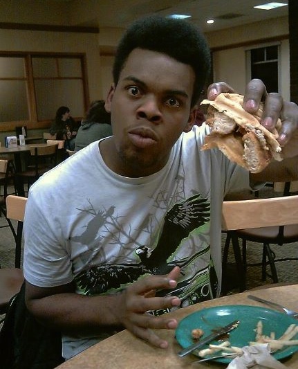 Caption: Brentton eating a chicken and waffle sandwich