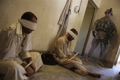 Caption: A US soldier guards detainees outside of Kirkuk., Credit: Associated Press