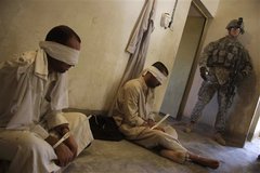 Caption: A US soldier guards detainees outside of Kirkuk., Credit: Associated Press