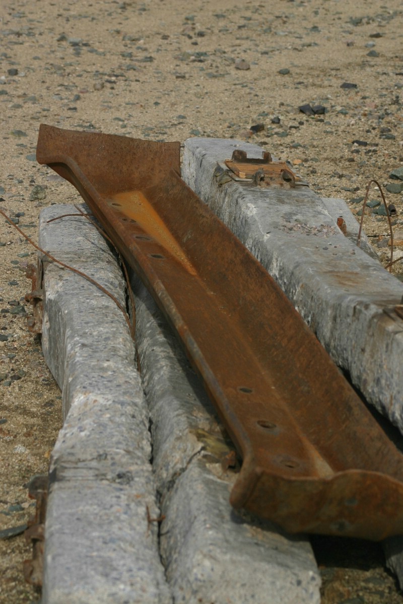 A Steel tie sits on top of a pile of concrete ties