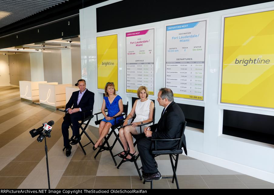 Telemundo/NBCUniversal Reporters sitting behind Train Schedule Displays