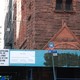 The graffitti, covered up by black paint, is next to the sign that announces the church's pending sale.