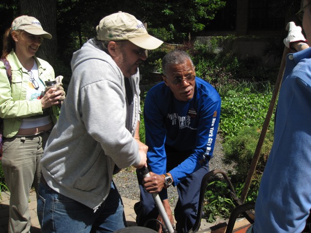 City Council Member Robert Jackson helps community volunteers pump a wheelbarrow's tire.