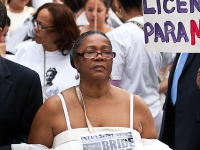 A woman marched on Sunday while wearing a wedding gown and holding a newspaper reporting the death of a woman at the hands of her partner.