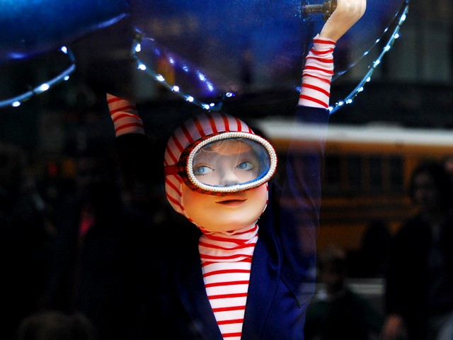 A little boy swings from a mechanical octopus in the window of Saks Fifth Avenue.