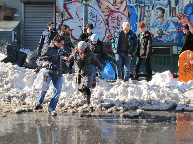 People crossed over a snow bank to avoid passing through the puddle.
