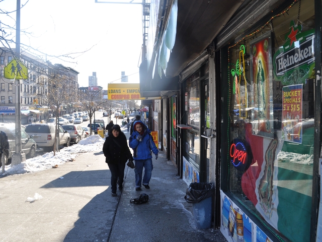 Residents walk into the bodega where a 20-year-old man was stabbed to death on the sidewalk outside on Friday.