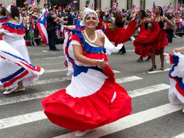 A woman in colorful dress dances along the parade route.