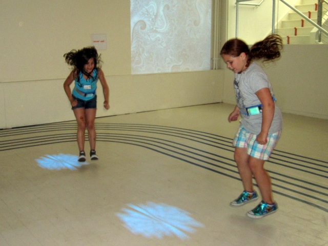 Kids follow moving lights on the floor, jumping to land in the center of them.