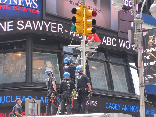 Police place a ladder to help coax an identified man into coming down from atop a light post in Times Square on Tuesday.