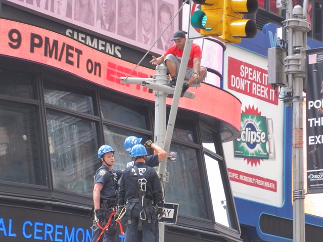 Unidentified man talks with NYPD while perched on traffic signal post.