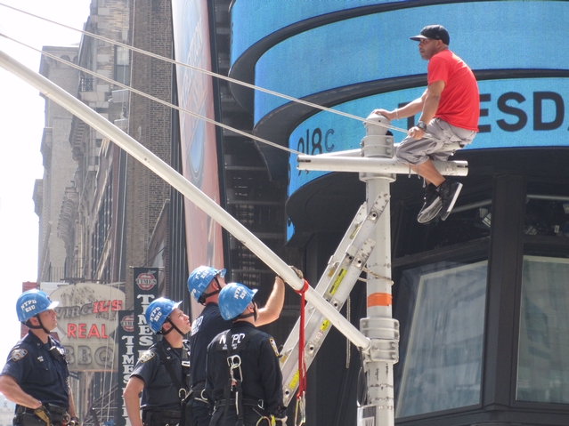 Police attempt to coax an unidentified man down from atop a traffic light pole in Times Square on Tuesdsay, June 28.