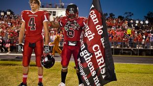 As two Kountze football players prepare to play a game on Oct. 5, 2012, one holds a banner with a Bible verse. A Hardin County judge recently ruled that the high school's cheerleaders can continue to display signs with religious messages at football games.