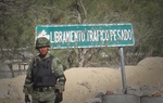 A solider guarding a checkpoint in Ciudad Mier stands in front of a sign riddled with bullet holes.