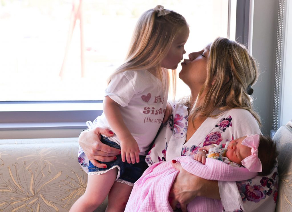 Hadley Burford gets a kiss from her mom as Elésha Burford holds Eloise, the first baby ever born in Highlands Ranch, CO.