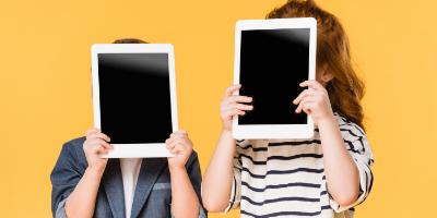 Two school aged children holding tablets in front of their faces.