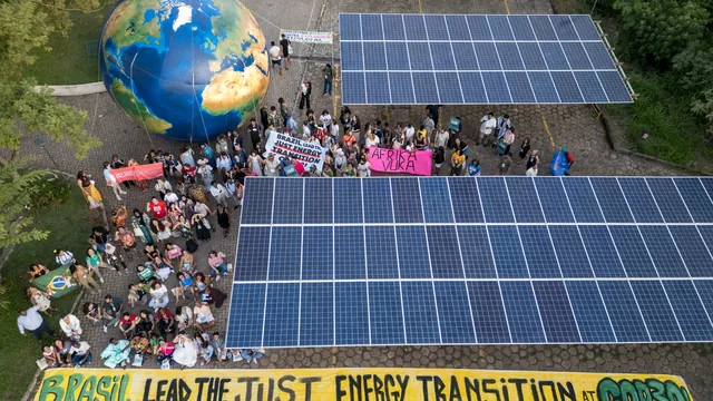 Aerial view of climate protesters gathered around a large Earth globe and solar panels, holding banners calling for just energy transition.