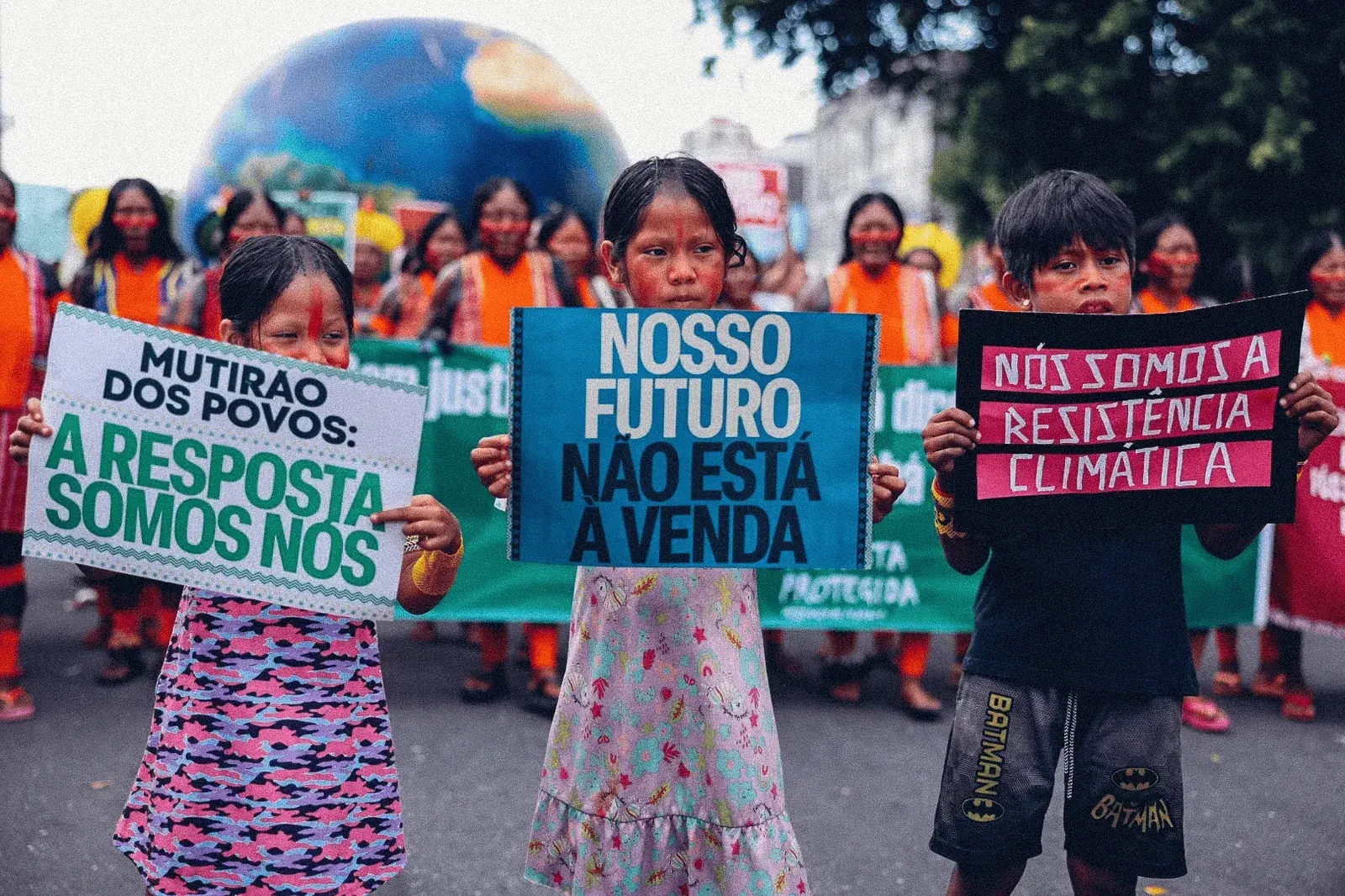 Young indigenous children lead a climate protest march, holding signs: "Our future is not for sale" and "We are the climate resistance"