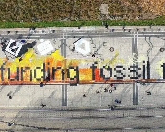Aerial photo of an artwork on train tracks that says "Stop funding fossil fuels"