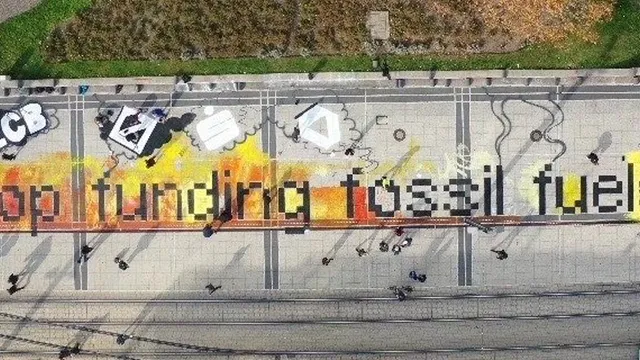 Aerial photo of an artwork on train tracks that says "Stop funding fossil fuels"
