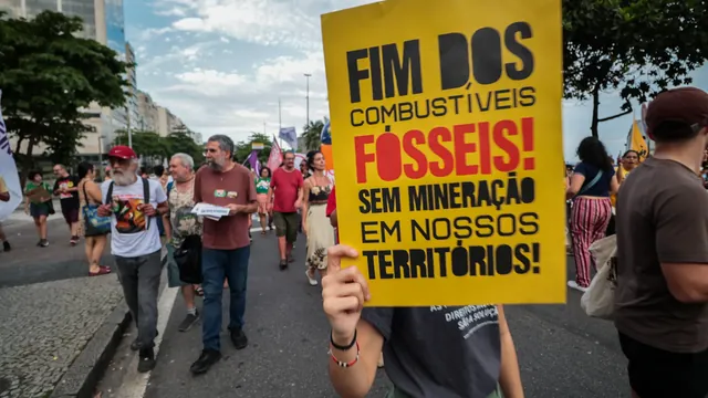 Protestor holding sign "fim dos combustiveis fosseis" during a larger march..