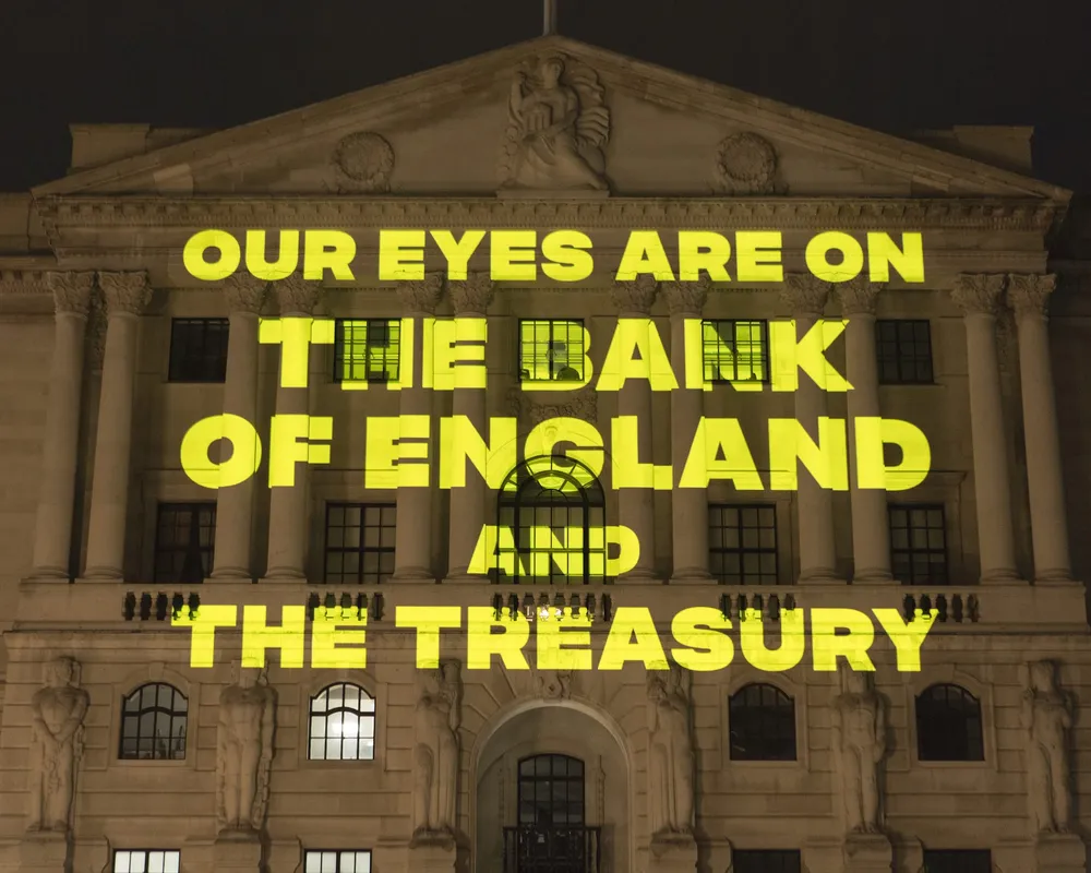 Yellow text reading "Our eyes are on the Bank of England and the Treasury' being projected onto the Bank of England at night-time
