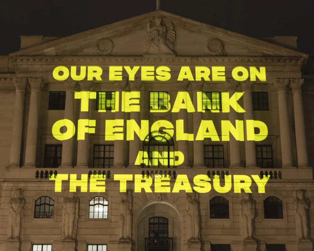 Yellow text reading "Our eyes are on the Bank of England and the Treasury' being projected onto the Bank of England at night-time