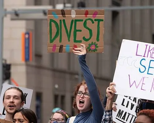 Students protesting and holding up signs saying "divest," and "like the sea, we rise."
