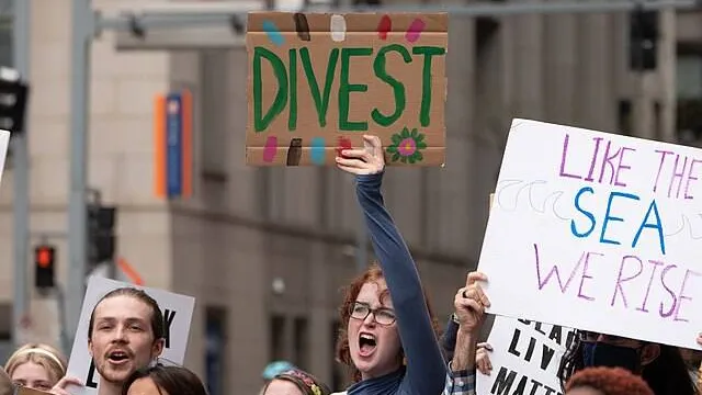 Students protesting and holding up signs saying "divest," and "like the sea, we rise."