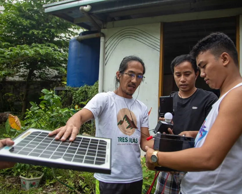 Three men construct a portable solar planel during a community-centred energy project in Tacloban, Philippines