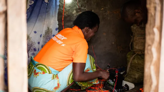 Mukabarungyi Jolene is connecting wires to power on solar light bulb inside her hut.