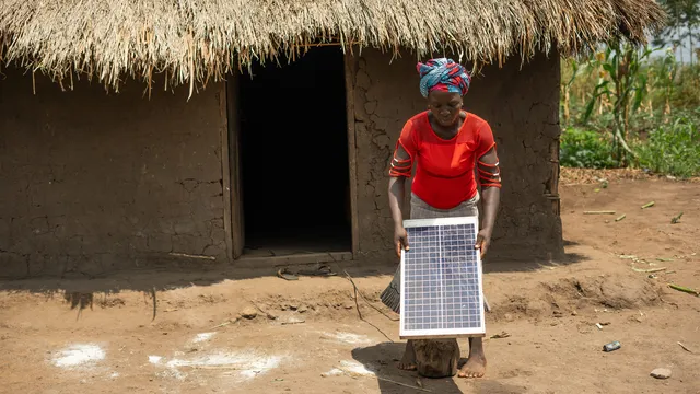 Annet Chantal, a farmer living in Kijumba village, outside of home with solar panel.
