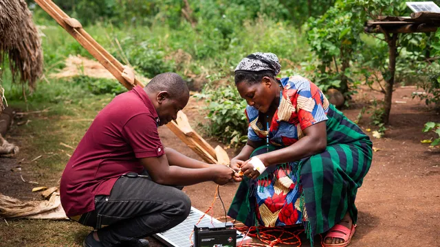 Edwin Mumbere, director of the Centre for Citizens Conserving Environment & Management (CECIC), training a woman of Kijumba on how to connect the solar panel to a battery.